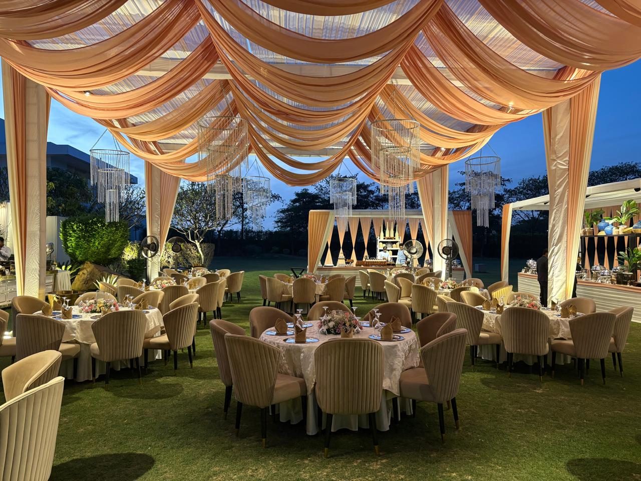 Draped peach pergola with chandeliers over outdoor dining tables